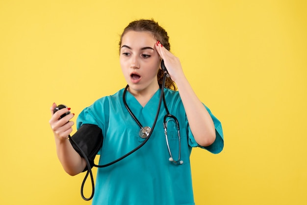 Vorderansicht Ärztin im medizinischen Hemd prüft ihren Druck auf gelbe Schreibtischvirus-Gesundheitsemotionsuniform-Covid-19-Pandemie
