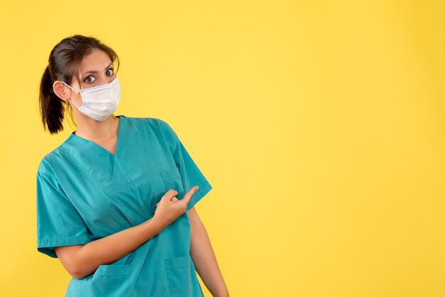 Vorderansicht-Ärztin im medizinischen Hemd und in der Maske auf gelbem Hintergrund