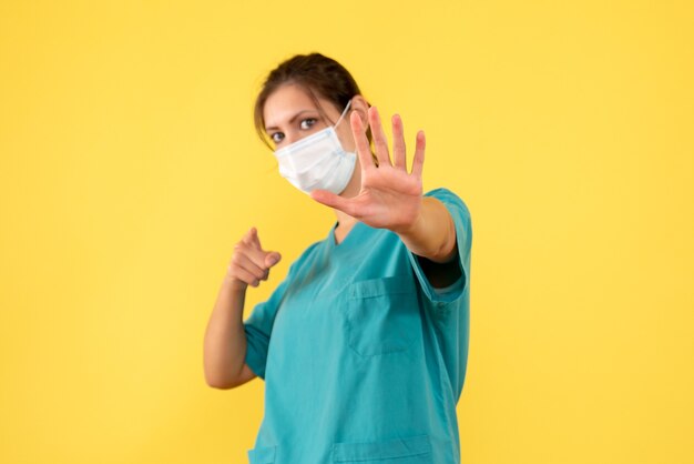 Vorderansicht-Ärztin im medizinischen Hemd und in der Maske auf gelbem Hintergrund