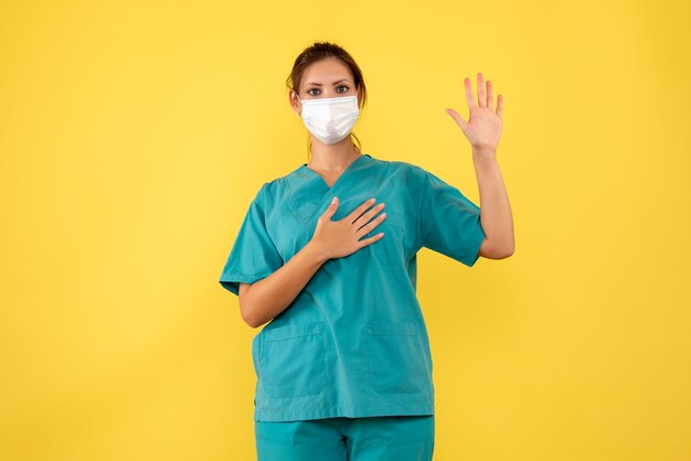 Vorderansicht-Ärztin im medizinischen Hemd und in der Maske auf gelbem Hintergrund