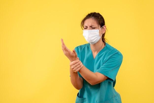 Vorderansicht-Ärztin im medizinischen Hemd und in der Maske verletzte ihre Hand auf gelbem Hintergrund