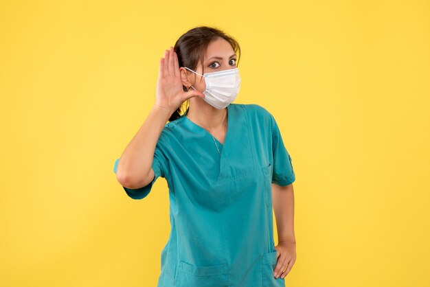 Vorderansicht-Ärztin im medizinischen Hemd und in der sterilen Maske auf gelbem Hintergrund