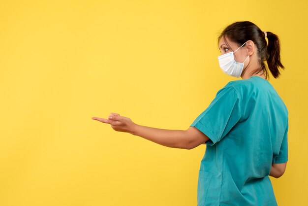 Vorderansicht-Ärztin im medizinischen Hemd und in der sterilen Maske auf gelbem Hintergrund