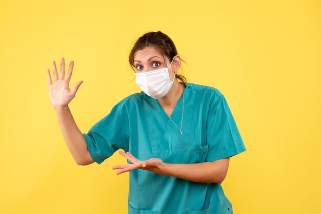 Vorderansicht-Ärztin im medizinischen Hemd und in der sterilen Maske auf gelbem Hintergrund