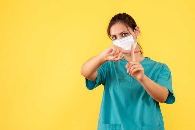 Vorderansicht Ärztin im medizinischen Hemd und mit steriler Maske auf gelbem Hintergrund