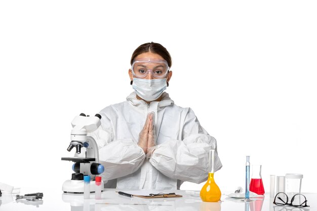 Vorderansicht Ärztin im Spezialanzug und mit Maske sitzend mit Lösungen auf weißem Hintergrund Covid-Virus-Pandemie-Coronavirus
