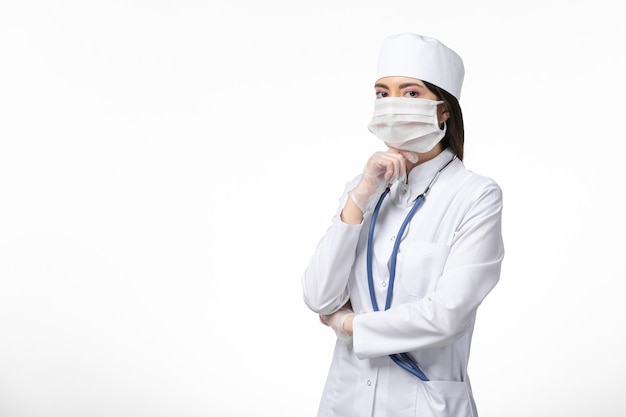 Vorderansicht Ärztin im weißen medizinischen Anzug mit einer Maske aufgrund des Coronavirus-Denkens auf der weißen Wandgesundheitskrankheit Pandemie covid-