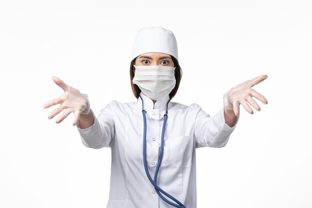 Vorderansicht Ärztin im weißen medizinischen Anzug mit einer Maske wegen Coronavirus auf weißer Wand Gesundheit Krankheit Pandemie covid-