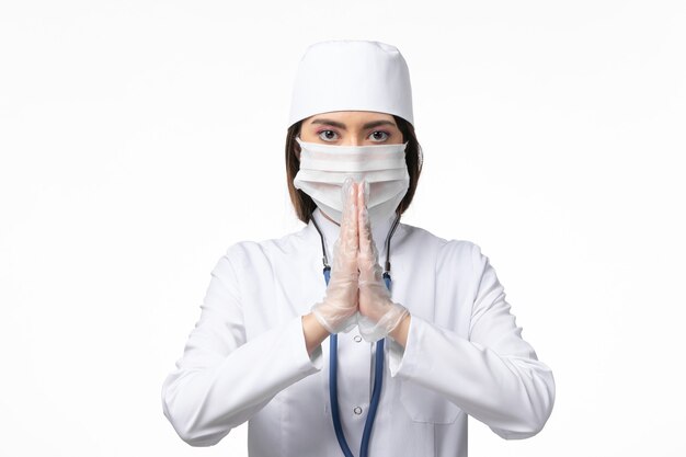 Vorderansicht Ärztin im weißen medizinischen Anzug mit einer Maske wegen Coronavirus auf weißer Wandkrankheit Medizinvirus covid-