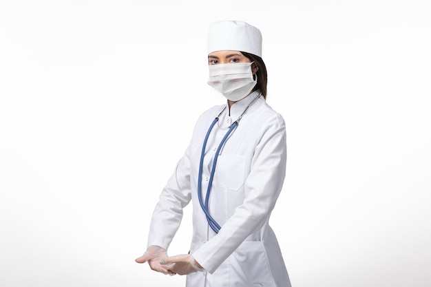 Vorderansicht Ärztin im weißen medizinischen Anzug mit einer Maske wegen Coronavirus auf White Wall Medicine Virus Pandemie Covid-