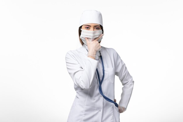 Vorderansicht Ärztin im weißen medizinischen Anzug mit einer Maske wegen Pandemie auf der hellweißen Wand Medizin Pandemie-Virus covid-