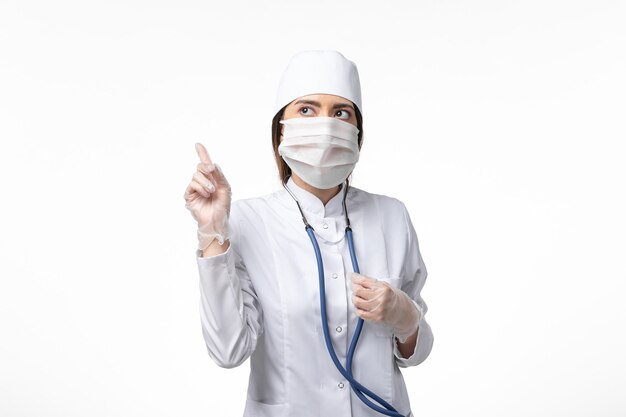 Vorderansicht Ärztin im weißen medizinischen Anzug mit einer Maske wegen Pandemie auf Lichtwandkrankheit Medizin Virus Pandemie covid-
