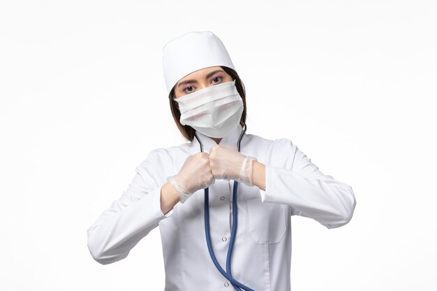 Vorderansicht Ärztin im weißen medizinischen Anzug mit einer Maske wegen Pandemie auf weißer Schreibtischkrankheit Medizin Virus Pandemie covid-