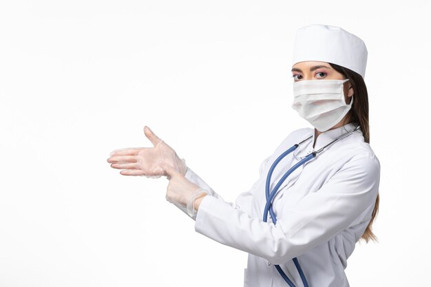 Vorderansicht Ärztin im weißen medizinischen Anzug mit einer Maske wegen Pandemie tragen Handschuhe auf weißen Schreibtischkrankheit Medizin Virus Pandemie covid-