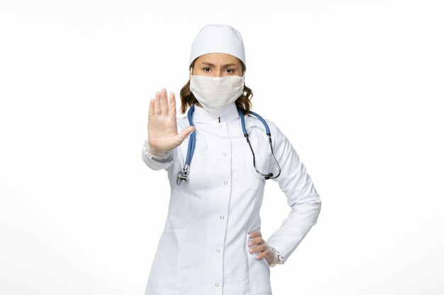 Vorderansicht Ärztin im weißen medizinischen Anzug und im Tragen der Maske wegen Coronavirus auf weißer Wand Pandemie Krankheit Isolation covid