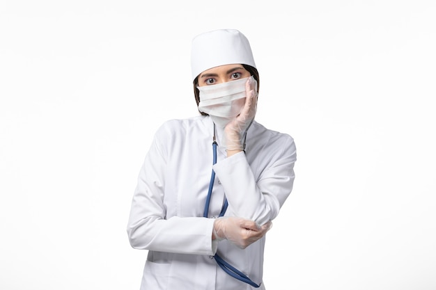 Vorderansicht Ärztin im weißen sterilen medizinischen Anzug mit Maske aufgrund des Coronavirus-Denkens auf dem Virus der weißen Schreibtischkrankheit Covid-Pandemic Disease