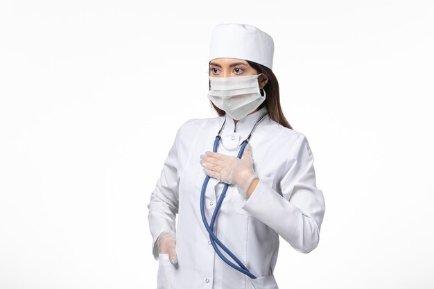 Vorderansicht Ärztin im weißen sterilen medizinischen Anzug mit Maske wegen Coronavirus bei weißer Wandkrankheit Covid-Pandemie-Virus-Krankheit