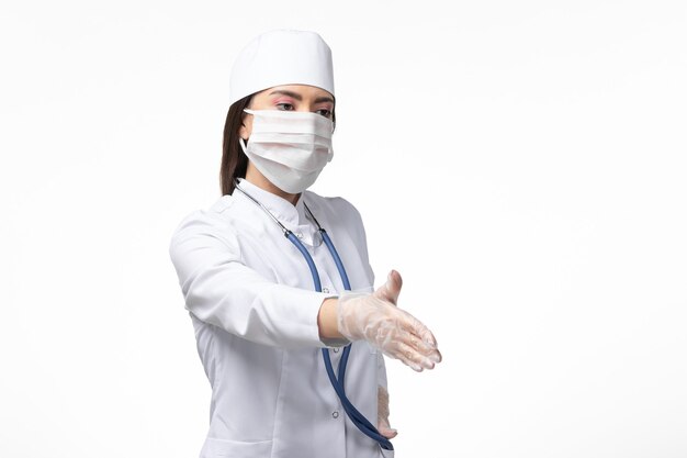 Vorderansicht Ärztin im weißen sterilen medizinischen Anzug mit Maske wegen Coronavirus Händeschütteln auf weißem Schreibtischkrankheit Covid-Pandemic Disease Virus