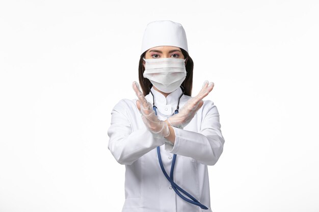 Vorderansicht Ärztin im weißen sterilen medizinischen Anzug mit Maske wegen Covid-zeigt Verbotszeichen auf Weißwandkrankheit Covid-Pandemie-Virus-Krankheit
