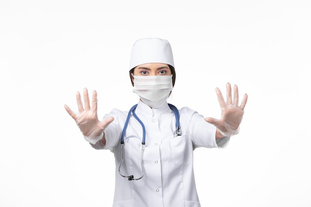 Vorderansicht Ärztin im weißen sterilen medizinischen Anzug und mit Maske aufgrund von Covid-Posing auf White-Wall-Disease-Virus-Covid-Pandemie-Krankheit