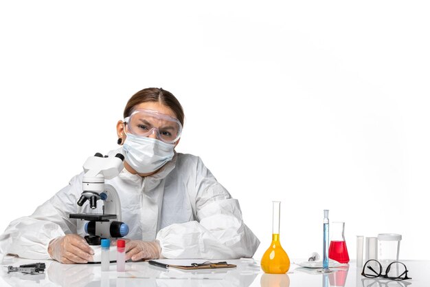Vorderansicht Ärztin in Spezialanzug und Maske unter Verwendung eines Mikroskops auf weißem Hintergrund Covid-Virus-Pandemie-Coronavirus