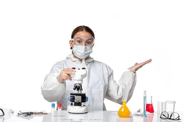 Vorderansicht Ärztin in Spezialanzug und tragende Maske mit Mikroskop auf hellweißem Hintergrund Covid Virus Pandemie Coronavirus