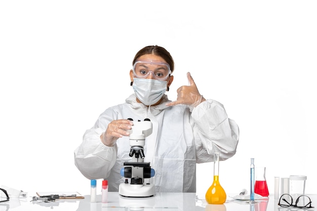 Vorderansicht Ärztin in Spezialanzug und tragende Maske mit Mikroskop auf weißem Hintergrund Covid Virus Pandemie Coronavirus arbeiten