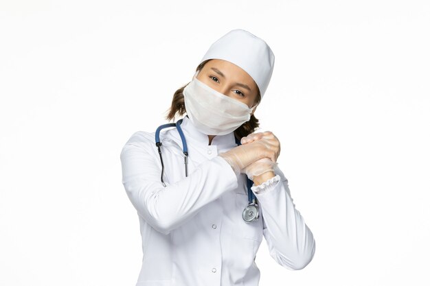 Vorderansicht Ärztin in weißem medizinischen Anzug und Maske auf weißer Wandpandemievirus-Krankheitskrankheitsmedizin