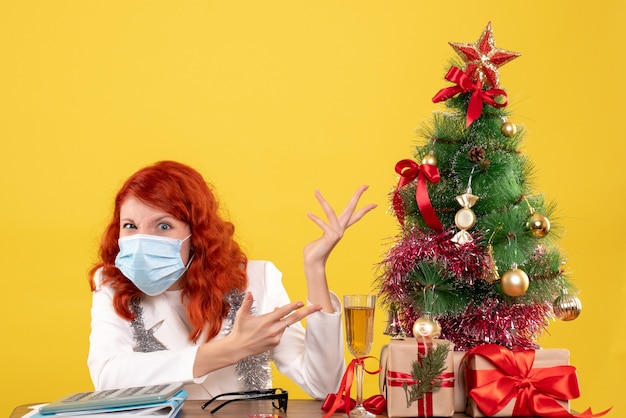 Vorderansicht Ärztin um Weihnachtsbaum und präsentiert sitzend in Maske