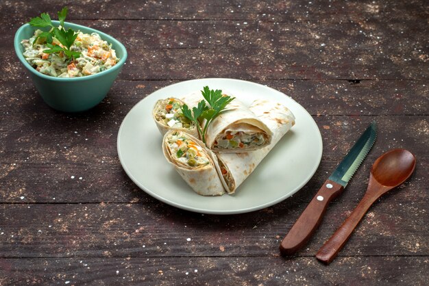 Vorderansicht Sandwichröllchen in Scheiben geschnitten mit Salat und Fleisch innen zusammen mit Mayyonaise Salat weiße Platte auf braun