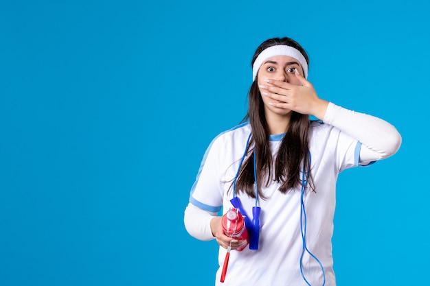 Vorderansicht schockierte hübsche Frau in Sportkleidung mit Flasche Wasser auf Blau