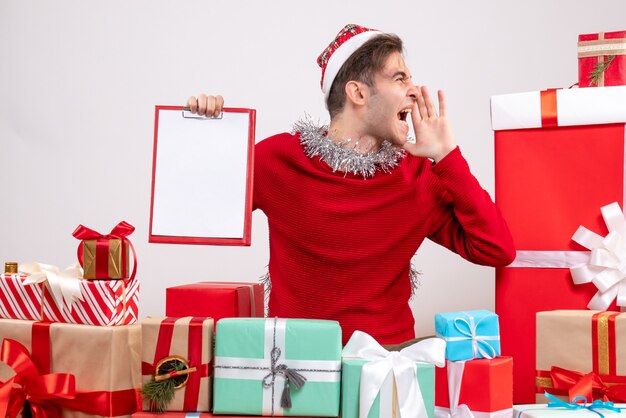 Vorderansicht schrie junger Mann Hoplding Zwischenablage sitzen um Weihnachtsgeschenke