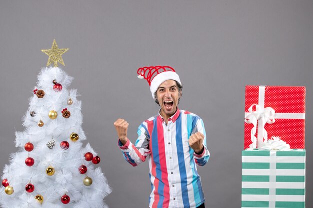Vorderansicht schrie Mann, der sein Glück mit Geste nahe Weihnachtsbaum zeigt