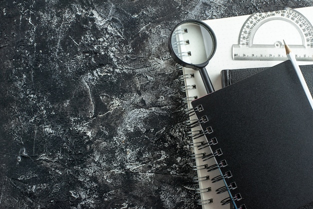 Kostenloses Foto vorderansicht schwarze schreibhefte mit stift und lupe auf grauem hintergrund notizblock college-schulstunde farbtafel-stiftheft