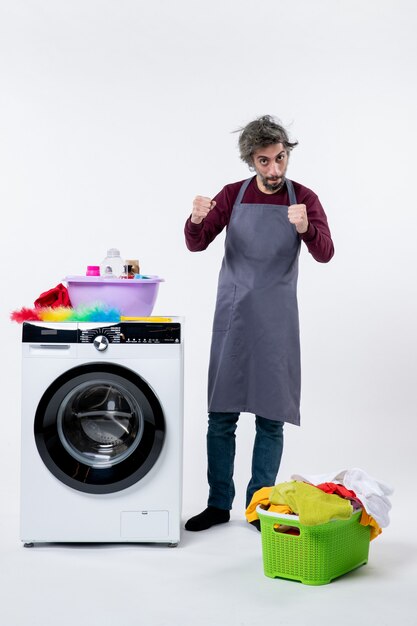 Vorderansicht selbstbewusster Haushältermann, der in der Nähe einer weißen Waschmaschine auf weißem Hintergrund steht