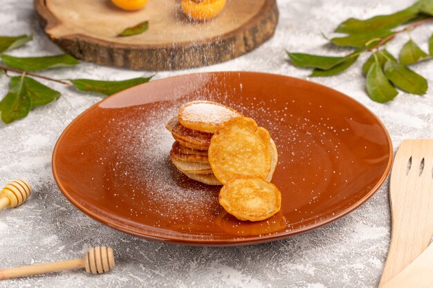 Vorderansicht süße köstliche Pfannkuchen innerhalb der braunen Platte auf dem süßen Dessert der grau-hellen Oberfläche Pfannkuchen-Mahlzeit Mahlzeit