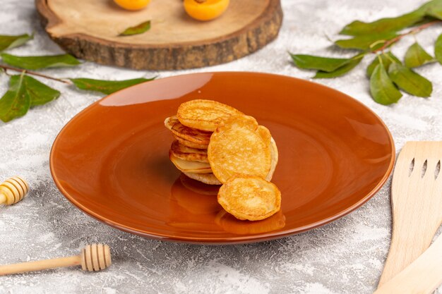 Vorderansicht süße köstliche Pfannkuchen innerhalb der braunen Platte auf dem süßen Nachtisch des grau-hellen Schreibtischpfannkuchen-Essensmahls