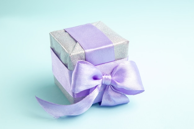 Vorderansicht süßes kleines Geschenk mit lila Schleife auf blauem Boden gebunden