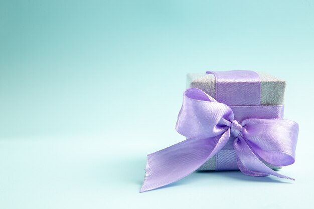 Vorderansicht süßes kleines Geschenk mit lila Schleife auf einem blauen Tisch gebunden