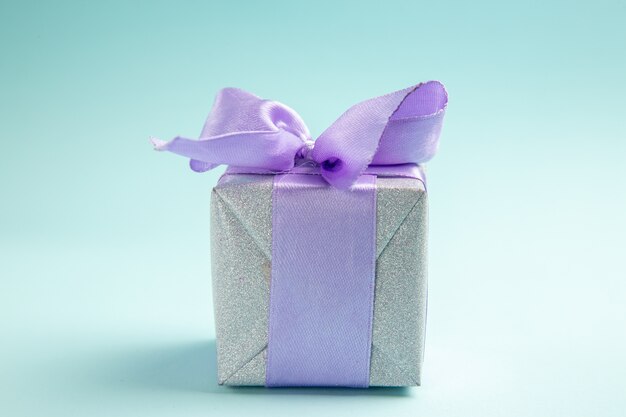 Vorderansicht süßes kleines Geschenk mit lila Schleife auf einem blauen Tisch gebunden