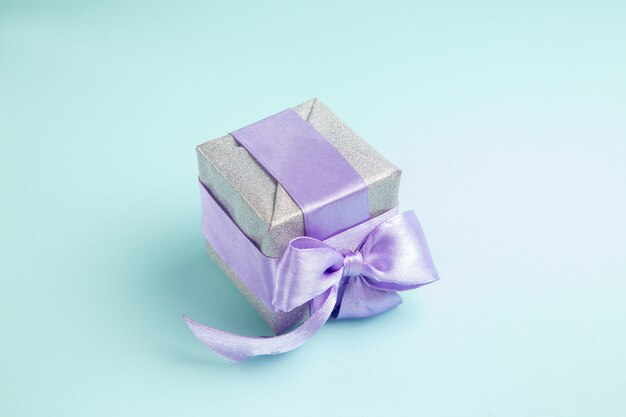 Vorderansicht süßes kleines Geschenk mit lila Schleife auf einem blauen Tisch gebunden