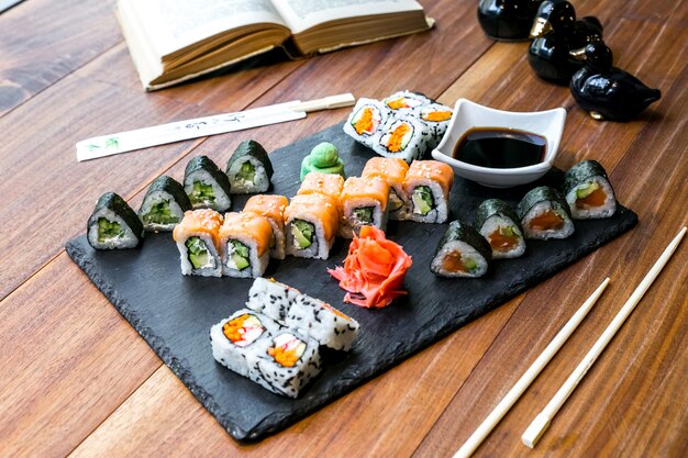 Vorderansicht Sushi-Set Brötchen mit Sojasauce Ingwer und Wasabi auf einem Teller und mit einem Buch auf dem Tisch
