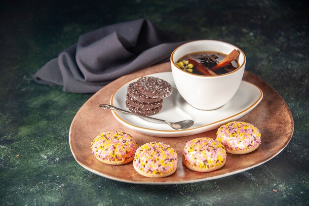 Vorderansicht Tasse Tee mit süßen Schoko-Keksen in Teller und Tablett auf dunkler Oberfläche Zeremonie Glas süße Frühstückstorte Dessert Farbe