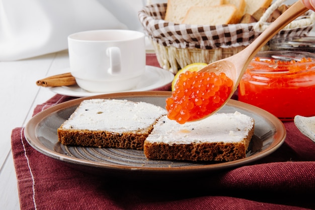 Vorderansicht Toast mit Butter und einem Löffel roten Kaviar auf einem Teller mit einer Tasse Tee