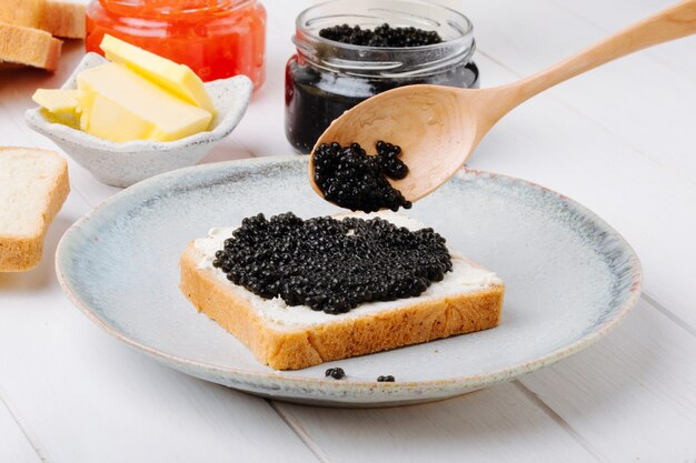 Vorderansicht Toast mit schwarzem Kaviar auf einem Teller mit einem Löffel und Butter mit einer Dose schwarzen und roten Kaviar