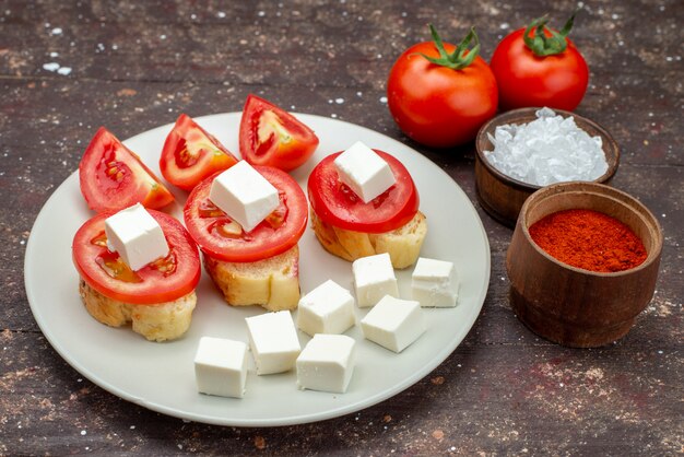 Vorderansicht Tomaten und Käse in weißer Platte mit Gewürzen auf braun