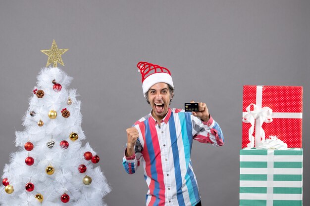 Vorderansicht überglücklicher Mann in einer siegreichen Geste, die nahe weißem Weihnachtsbaum steht