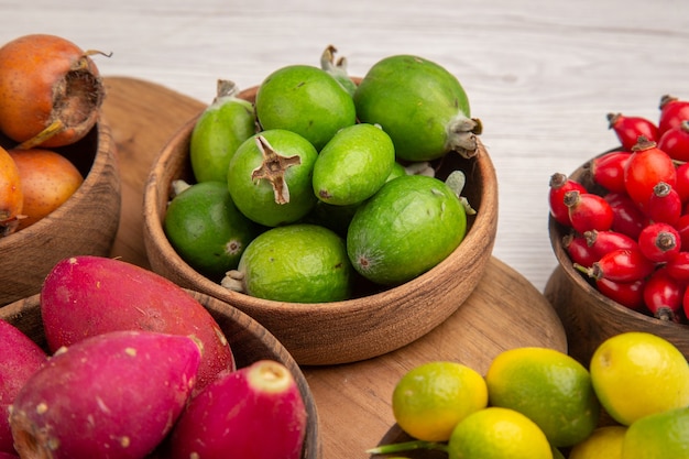 Vorderansicht verschiedene früchte feijoas beeren und andere früchte in tellern auf weißem schreibtisch reifes essen exotische tropische fotofarbe