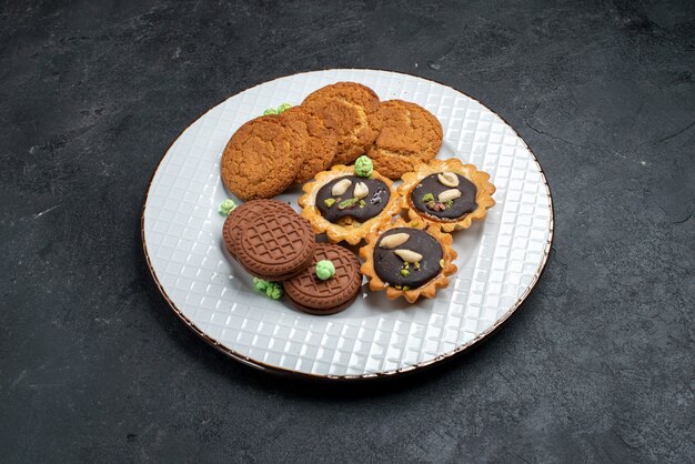 Vorderansicht verschiedene Kekse süße und köstliche Kekse innerhalb Platte auf grauer Oberfläche Keks backen Zucker süße Kuchen Kekse