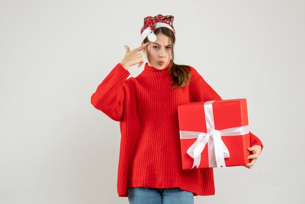 Vorderansicht verwirrte Mädchen mit Weihnachtsmütze, die Geschenkfingerpistole hält